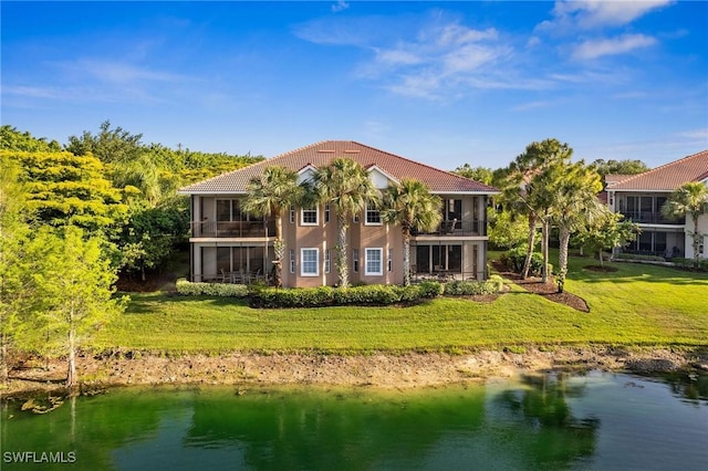 rear view of house featuring a lawn, a sunroom, a balcony, a water view, and stucco siding