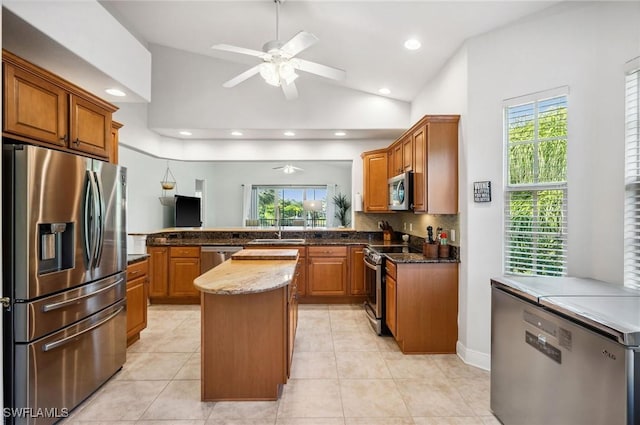 kitchen featuring appliances with stainless steel finishes, ceiling fan, high vaulted ceiling, dark stone countertops, and a kitchen island