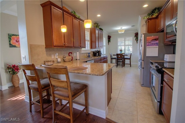 kitchen featuring stainless steel appliances, a kitchen breakfast bar, kitchen peninsula, pendant lighting, and ornamental molding