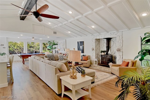 living room with ceiling fan, light wood-type flooring, lofted ceiling with beams, and a wood stove