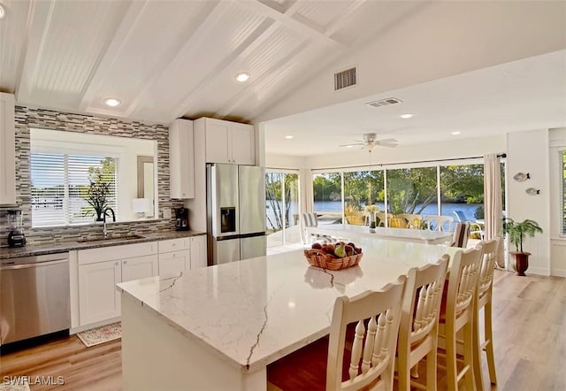 kitchen with a kitchen breakfast bar, stainless steel appliances, light stone counters, white cabinetry, and tasteful backsplash