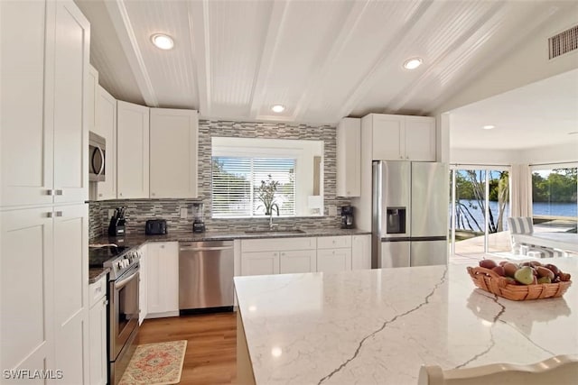 kitchen featuring appliances with stainless steel finishes, sink, light stone counters, white cabinets, and tasteful backsplash