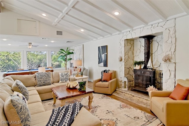 living room with light hardwood / wood-style floors, lofted ceiling with beams, ceiling fan, and a wood stove