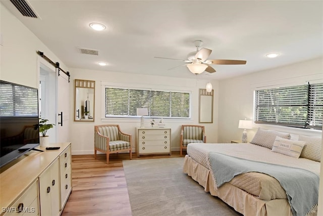 bedroom featuring ceiling fan, a barn door, and light hardwood / wood-style floors