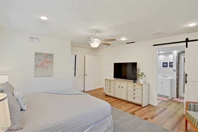 bedroom featuring sink, ensuite bathroom, ceiling fan, light wood-type flooring, and a barn door