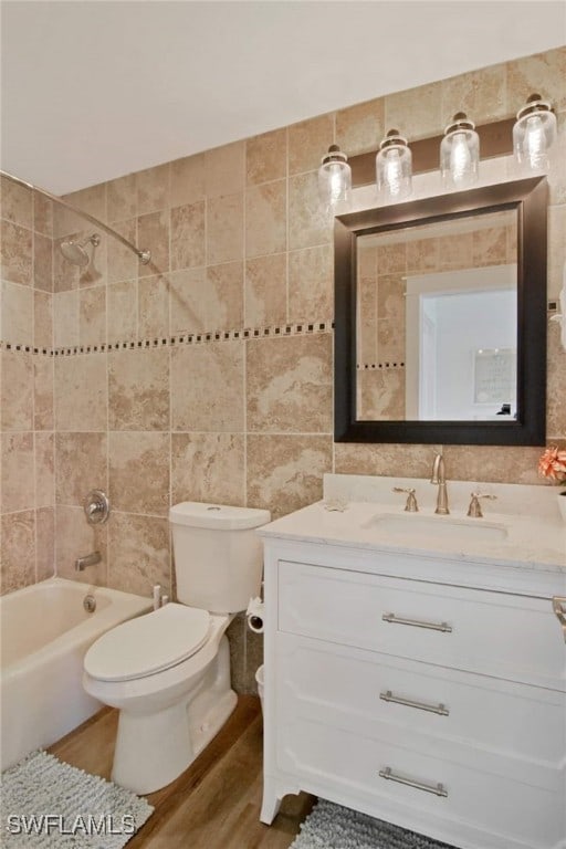 full bathroom with tile walls, hardwood / wood-style floors, toilet, vanity, and tiled shower / bath combo