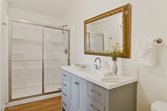 bathroom with vaulted ceiling, a shower with shower door, toilet, wood-type flooring, and vanity