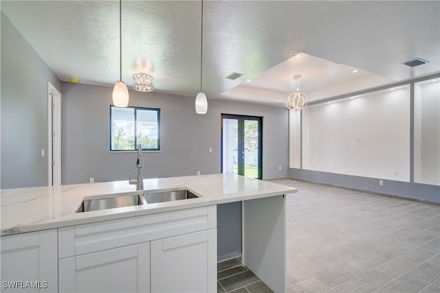 kitchen featuring light stone counters, a raised ceiling, sink, white cabinetry, and hanging light fixtures