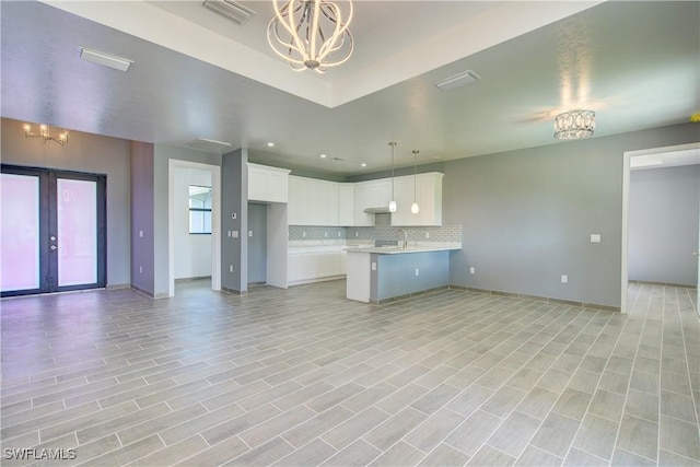 kitchen featuring white cabinetry, backsplash, kitchen peninsula, pendant lighting, and a chandelier