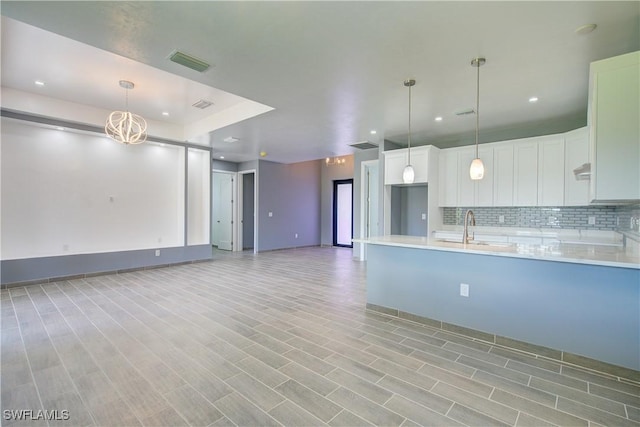 kitchen featuring backsplash, sink, white cabinets, and decorative light fixtures