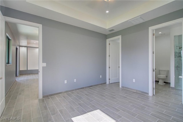 unfurnished bedroom featuring ensuite bathroom and a tray ceiling