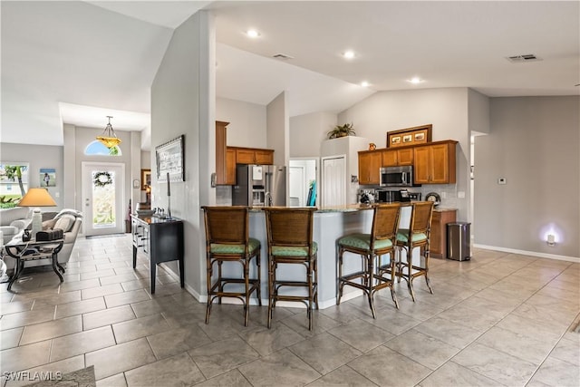 kitchen with kitchen peninsula, vaulted ceiling, a kitchen bar, light tile patterned flooring, and appliances with stainless steel finishes