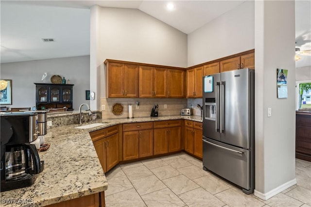 kitchen with light stone countertops, sink, high end refrigerator, kitchen peninsula, and decorative backsplash