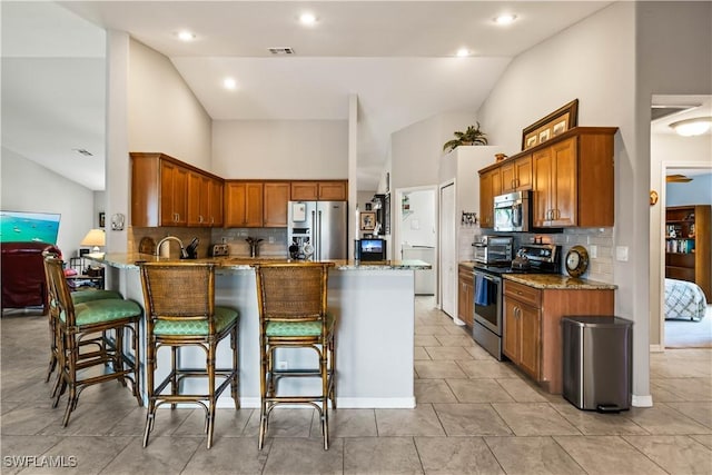 kitchen with backsplash, kitchen peninsula, a kitchen bar, and appliances with stainless steel finishes