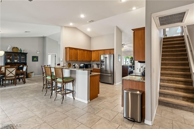 kitchen featuring kitchen peninsula, stainless steel refrigerator with ice dispenser, a kitchen bar, ceiling fan, and high vaulted ceiling