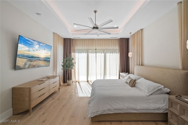 bedroom featuring light hardwood / wood-style flooring, a raised ceiling, and ceiling fan