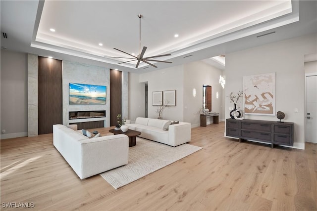 living room with light wood-type flooring, a fireplace, and a tray ceiling