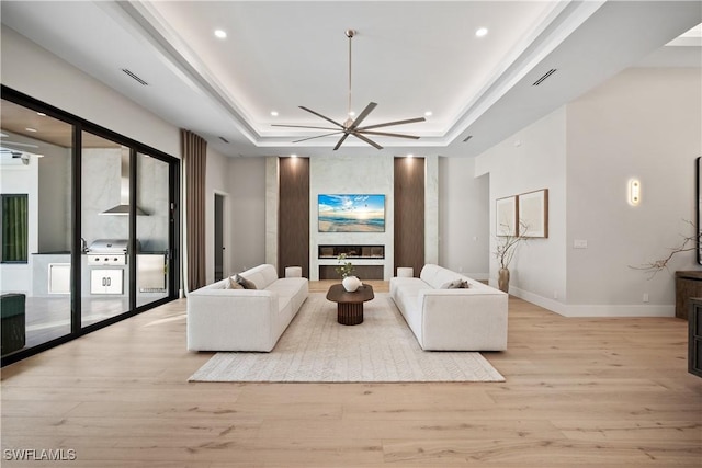 living room featuring a fireplace, light wood-type flooring, a raised ceiling, and ceiling fan