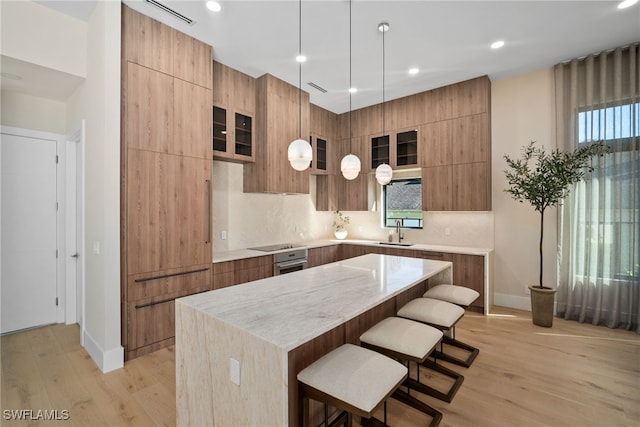 kitchen featuring light stone counters, sink, light hardwood / wood-style flooring, a kitchen island, and hanging light fixtures