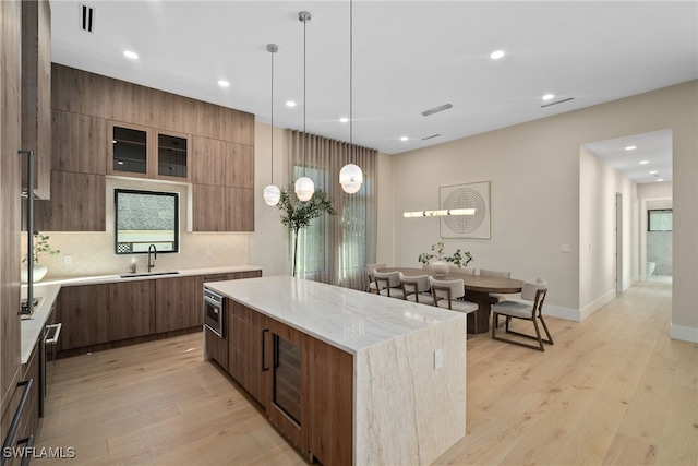 kitchen featuring sink, hanging light fixtures, light hardwood / wood-style floors, decorative backsplash, and a kitchen island