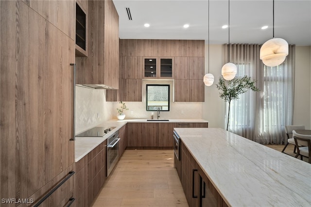 kitchen featuring light stone countertops, black electric cooktop, sink, pendant lighting, and oven