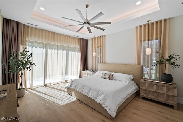 bedroom with light hardwood / wood-style flooring, a raised ceiling, and ceiling fan