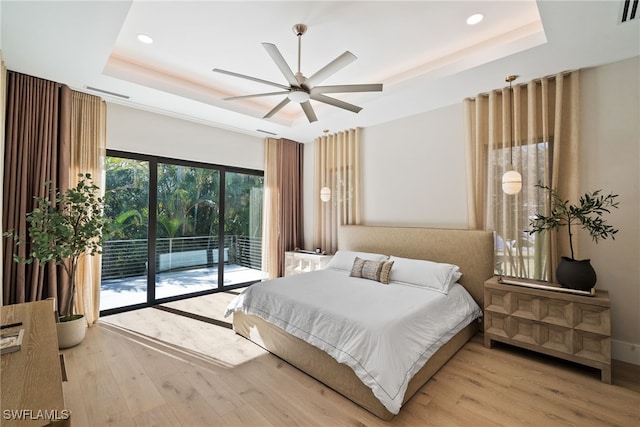 bedroom with ceiling fan, light hardwood / wood-style floors, access to exterior, and a tray ceiling