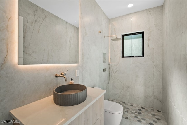 bathroom with a tile shower, sink, tile walls, and toilet