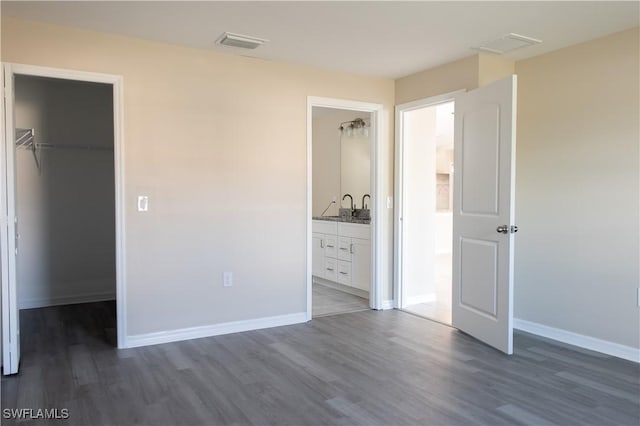 unfurnished bedroom featuring a walk in closet, a closet, ensuite bath, and dark hardwood / wood-style flooring