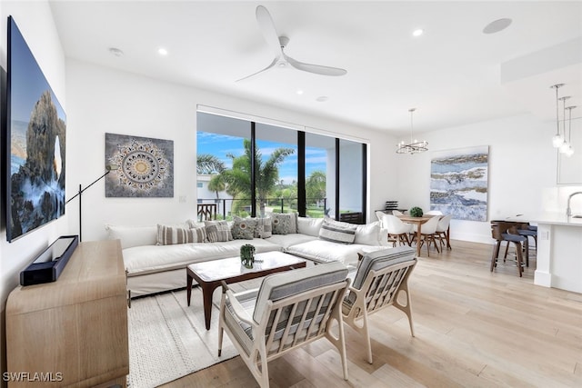 living room with ceiling fan with notable chandelier and light hardwood / wood-style flooring