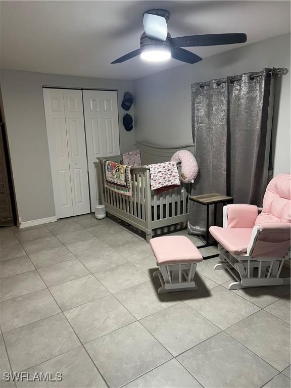 bedroom featuring ceiling fan, a crib, light tile patterned floors, and a closet