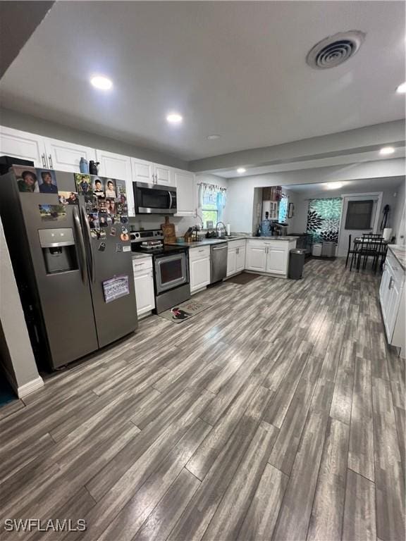 kitchen featuring white cabinets, wood-type flooring, kitchen peninsula, and appliances with stainless steel finishes