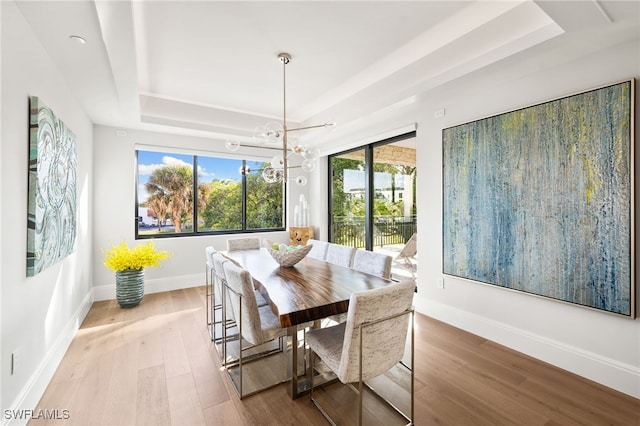 dining space with a chandelier, a tray ceiling, light wood-type flooring, and baseboards