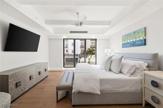 bedroom with light wood-type flooring, access to outside, baseboards, and a tray ceiling