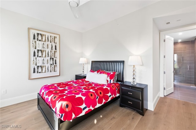 bedroom featuring ensuite bath, wood finished floors, visible vents, and baseboards