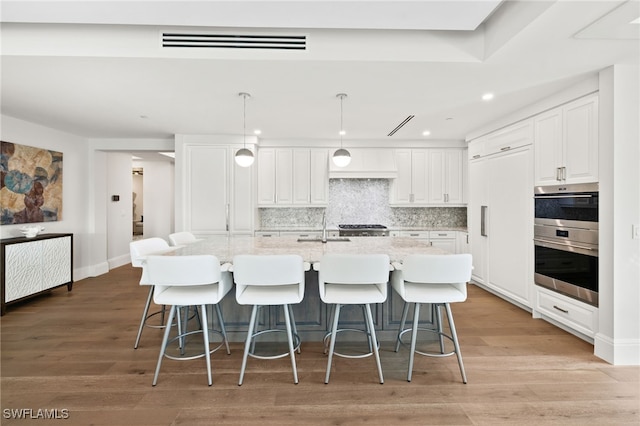 kitchen featuring a center island with sink, pendant lighting, white cabinets, and decorative backsplash