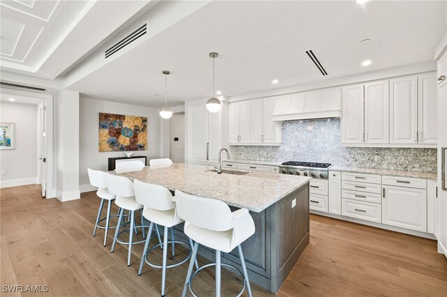 kitchen with white cabinets, sink, an island with sink, decorative light fixtures, and custom range hood