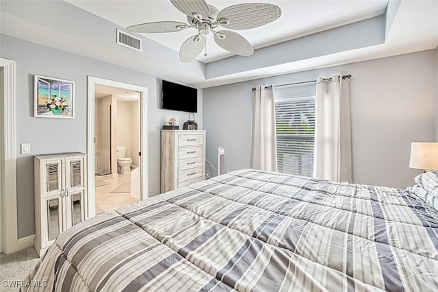 bedroom with ensuite bathroom, ceiling fan, light carpet, visible vents, and a raised ceiling