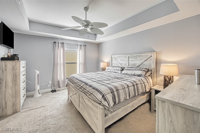 bedroom with light carpet, a tray ceiling, a ceiling fan, and baseboards