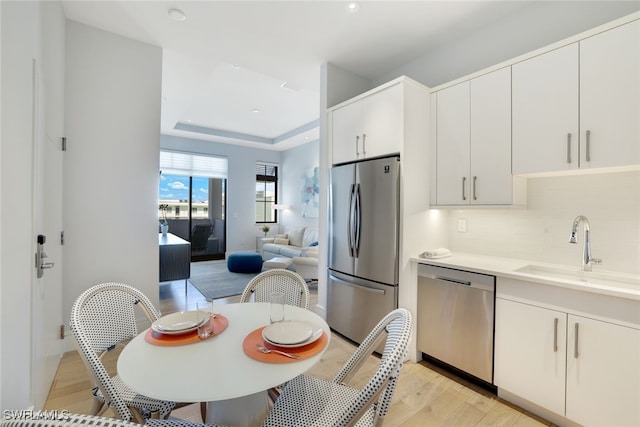 kitchen featuring white cabinetry, sink, tasteful backsplash, light hardwood / wood-style floors, and appliances with stainless steel finishes