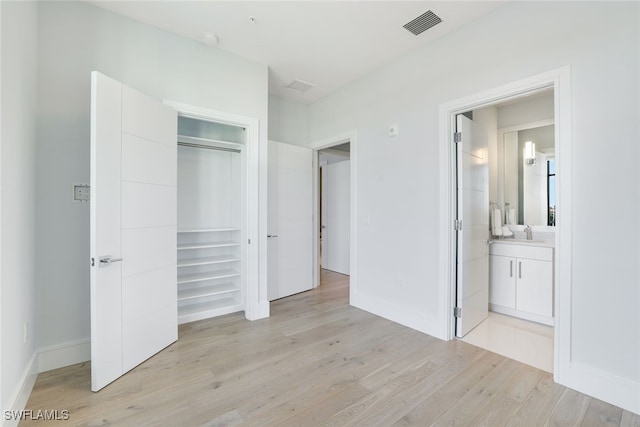 unfurnished bedroom featuring light hardwood / wood-style floors, ensuite bath, a closet, and sink