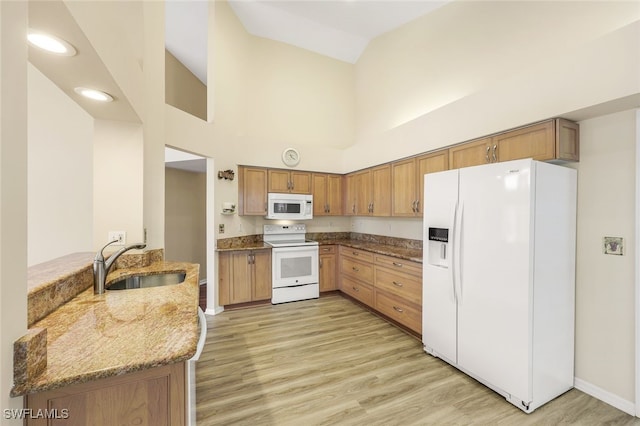 kitchen with light stone countertops, sink, kitchen peninsula, a towering ceiling, and white appliances