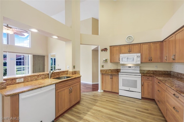 kitchen featuring kitchen peninsula, white appliances, sink, stone countertops, and high vaulted ceiling