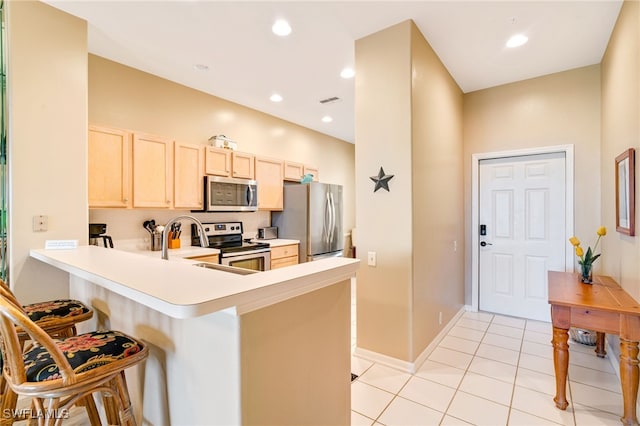 kitchen with kitchen peninsula, appliances with stainless steel finishes, light brown cabinetry, a breakfast bar, and light tile patterned floors