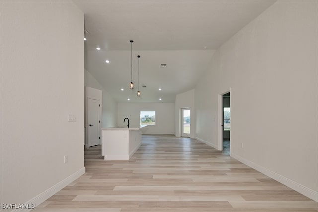interior space featuring pendant lighting, high vaulted ceiling, sink, an island with sink, and light hardwood / wood-style floors