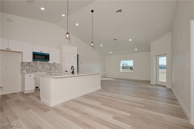 kitchen featuring white cabinetry, high vaulted ceiling, decorative light fixtures, decorative backsplash, and a center island with sink