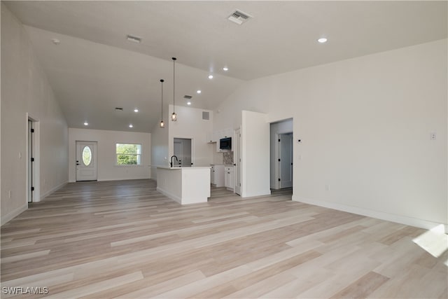 kitchen with light wood-type flooring, a kitchen island with sink, pendant lighting, high vaulted ceiling, and white cabinetry