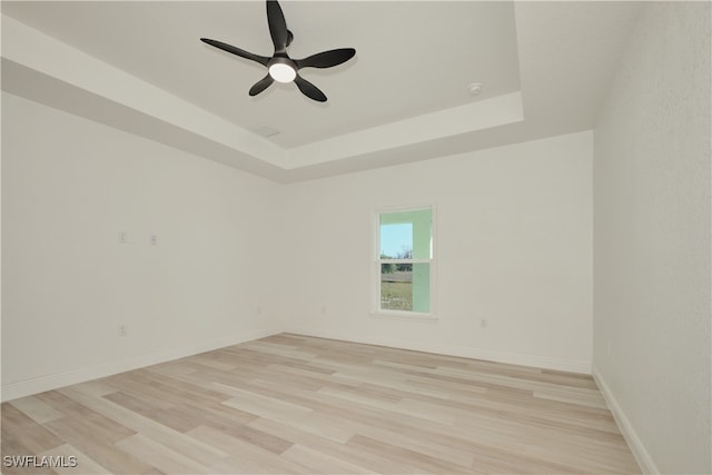 unfurnished room with a raised ceiling, ceiling fan, and light hardwood / wood-style floors