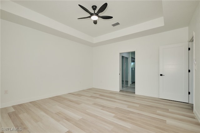 empty room featuring a tray ceiling, ceiling fan, and light hardwood / wood-style floors