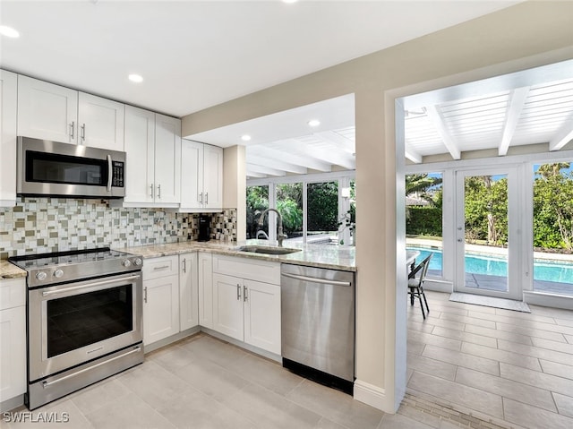 kitchen with beam ceiling, white cabinetry, sink, light stone counters, and appliances with stainless steel finishes